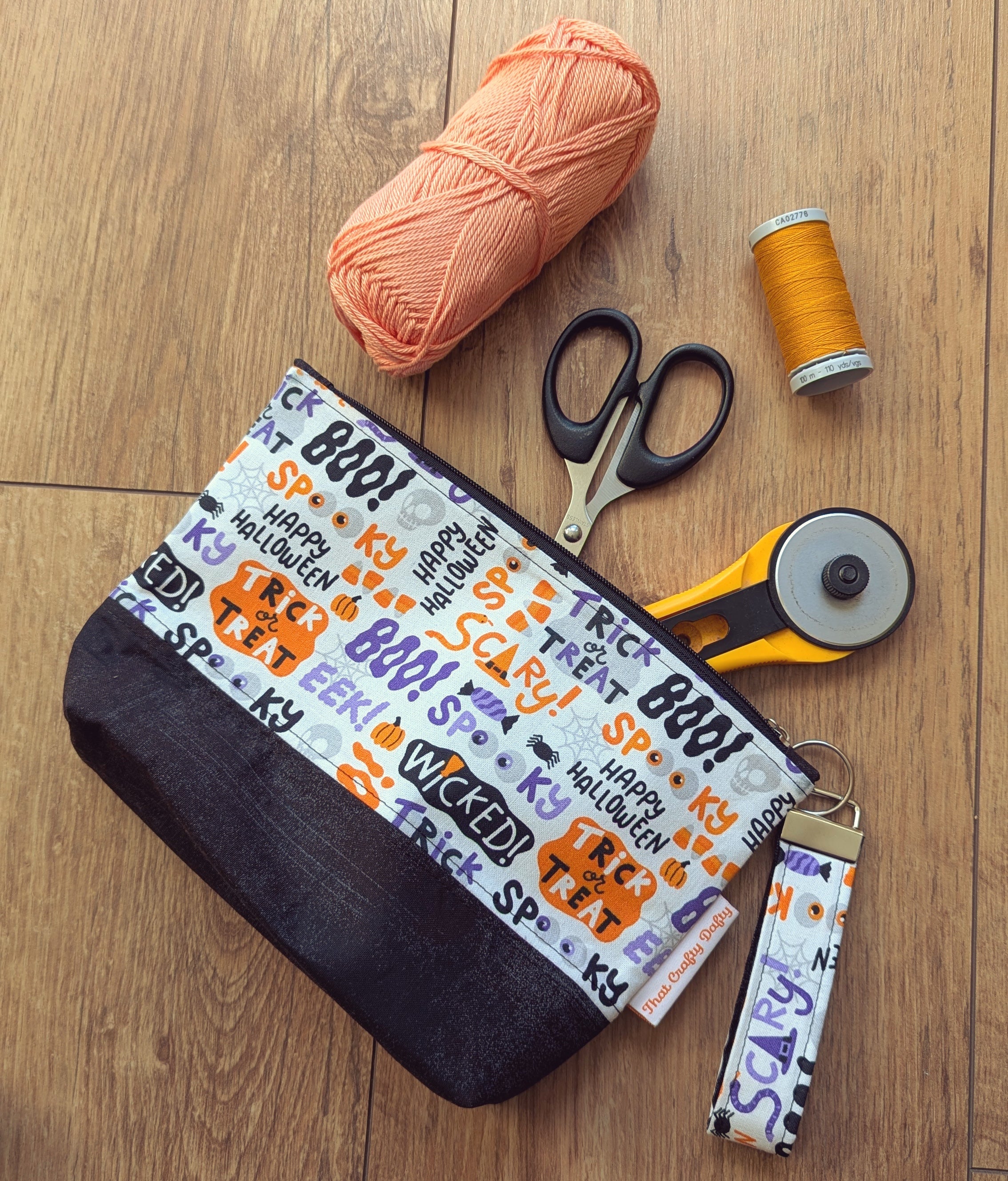 A handmade zipper pouch featuring some whimsical Halloween fabric, with a selection of crafty notions spilling out of it on to the floor. 